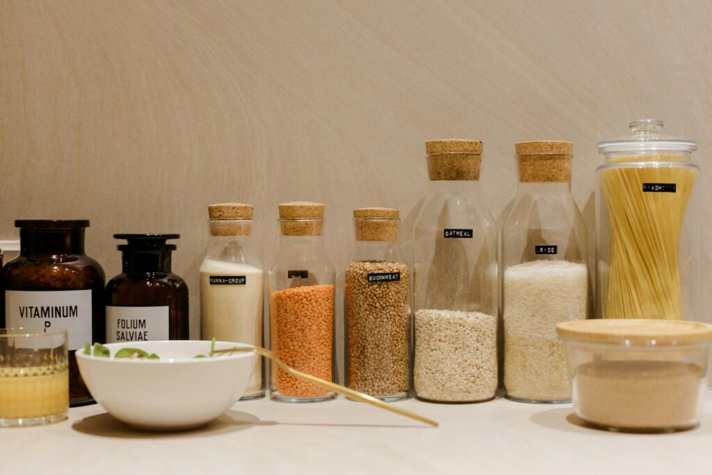 A variety of grains and pasta in labeled glass bottles displayed on a kitchen counter.